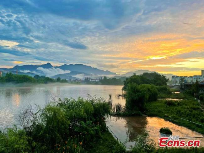 Η γέφυρα, ο ποταμός που ρέει, τα σπίτια και το ηλιοβασίλεμα, δημιουργούν ένα ποιητικό τοπίο μετά από μια δυνατή βροχή στην κομητεία Γιουάν’αν στην επαρχία Χουμπέι, στις 7 Ιουλίου 2021. (Φωτογραφία / Liu Zhongyi)